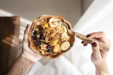 an overhead photo of a person's hands holding a bowl of yogurt with granola and banana slices