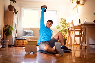 man doing a learning how to do a turkish get-up exercise on a tablet in his living room