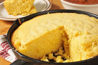 Cornbread in a skillet with a slice removed, served with chili on a table