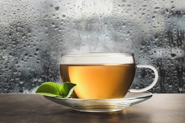 Glass cup of hot green tea near window on rainy day