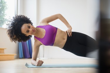 Person wearing purple sports bra and black leggings performing side Copenhagen plank in gym