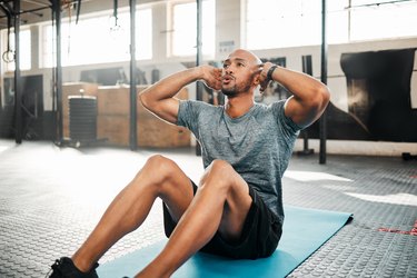 Person wearing a gray T-shirt and black shorts doing a sit-up in the gym