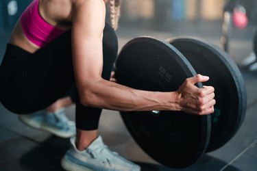 Person in gym loading weights onto a barbell, getting ready to perform a landmine exercise.