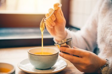 近距离的人勺子蜂蜜到白色的马克杯茶的好处与蜂蜜茶