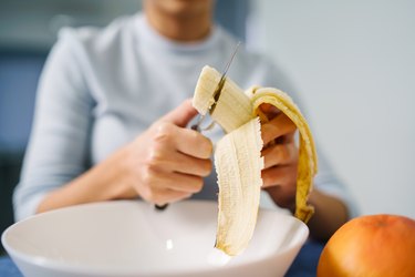 ]woman sitting by the table at home cutting banana with vitamins and minerals