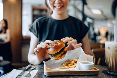 woman eating a burger and fries, as an example of foods to avoid with GERD