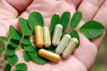 Close-Up Of Hand Holding olive leaf extract supplements and leaves