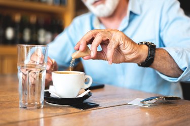 Senior man pouring sugar into coffee at restaurant
