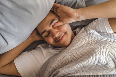 Lazy man rubbing eyes while lying on bed at home