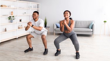 Fit black couple doing air squats, a beginner glute exercise, together in their living room