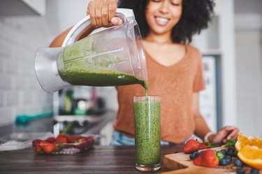 woman pouring a green fruit smoothie into a glass