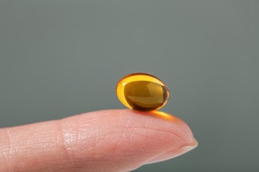 Female hand holding a small yellow capsule of nutritional supplement. Food supplement, vitamin D, omega, vitamin C.