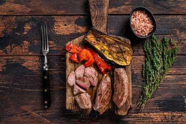 Broiled deer (venison) steaks, Fillet Meat steak on wooden cutting board. Dark wooden background. Top view