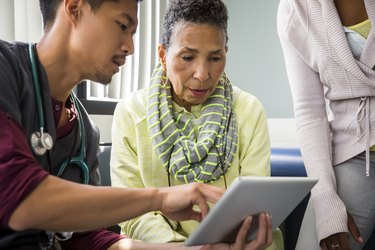 Male nurse showing digital tablet to senior woman by female in hospital