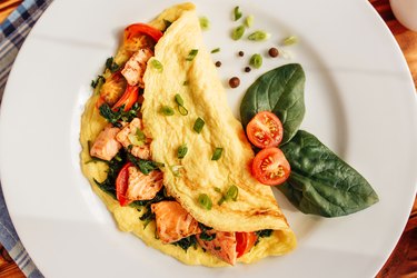 overhead photo of an omelet on a white plate made with spinach, tomato and salmon and topped with chives