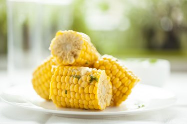sweet corn, a food high in glucose, on the cob, cut into sections on a plate served outside.