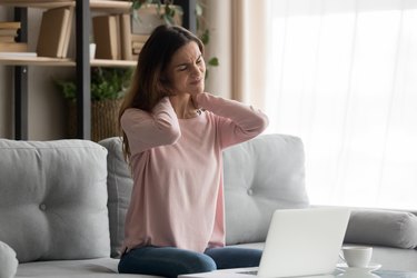 Woman sitting on couch near computer suffers from neck pain