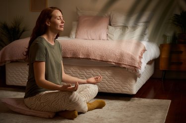 Smiling young woman meditating on the floor of her bedroom