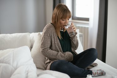 年轻女人生病在床上拿着一杯水。