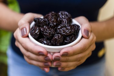 A woman holding a bowl of prunes as a natural remedy for constipation