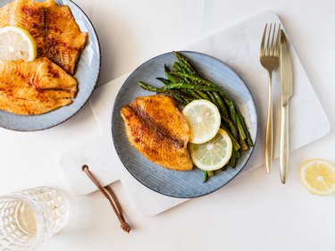 Top view of roasted tilapia fish with asparagus on a ceramic plate. Healthy mediterranean diet lunch or dinner