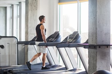 Person wearing tank top, shorts and sneakers walking on treadmill in gym for weight loss.