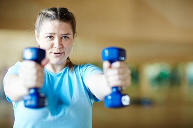 Woman doing front raises during a workout with dumbbells