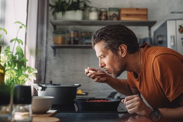 Man Tasting Sauce with a Mixing Spoon in a Kitchen, trying to eat more plants