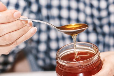a person's hand holding a glass jar of honey