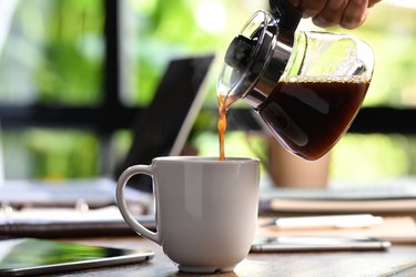 A hand pouring steaming coffee in to a cup on a work desk when work from home