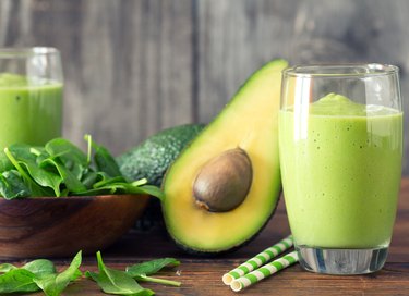 Green vocado smoothie recipe made with spinach in a glass on a wooden cutting board