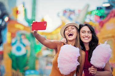 Happy girlfriends are taking selfie/making video call and make fun together in a fun fair