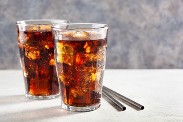 glass of cold fructose-rich cola soft drink on white table gray background