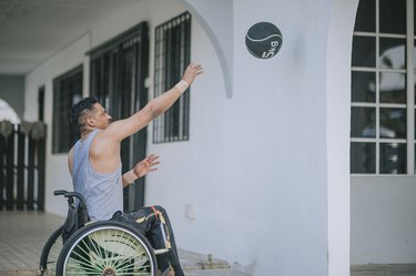 Person in wheelchair throwing a medicine ball against a wall at their house to build strength and power