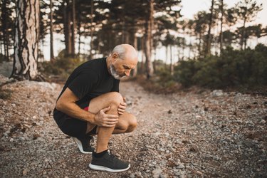 Senior man in the woods holding his knee because he is bruising more easily with age