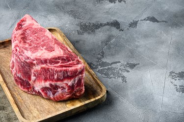 Raw boneless ribeye steak on wooden plate on grey stone background