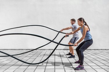 side view of a man and woman exercising with battle ropes in front of a white wall