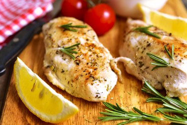 Roasted chicken breast with rosemary, lemon and tomatoes on a cutting board