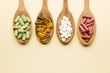 overhead photo of four types of supplement and vitamin pills in wooden spoons