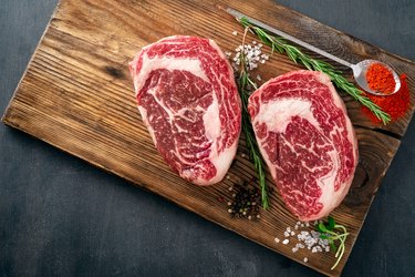 Two raw rib eye steak on the butcher's Board on a wooden table prepared prepared for cooking. Marbled beef top view