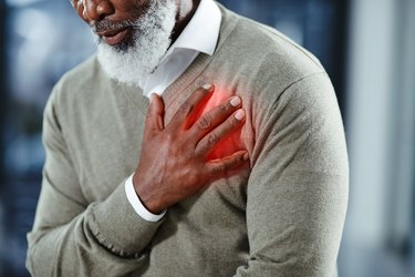 Close up photo of older adult wearing a grey sweater, putting his hand on his chest and showing where he has heartburn.