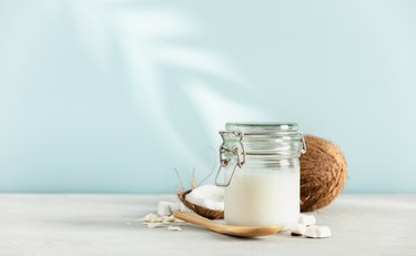 Coconut oil in jar with fresh coconut and tropical leaf shadow