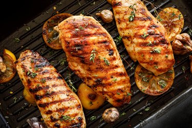 Grilled chicken cutlets with thyme, garlic and lemon slices on a grill pan close up