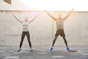 man and woman doing star jumps in front of a concrete wall