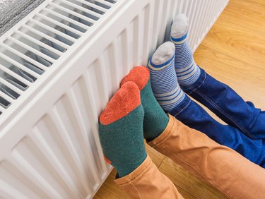 parent and child wearing colorful socks warming cold feet in front of radiator
