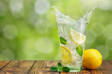 lemon slices in glass of splashing water on wooden table with green blurred background