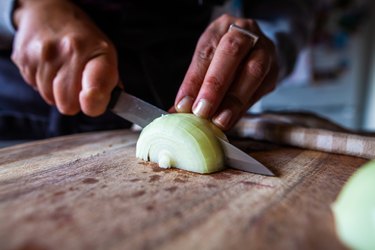 Close up of a person chopping an onion on a wooden cutting board and wondering if onions lower blood sugar