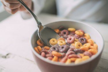 View from above of an unrecognizable person eating colorful ring-shaped cereal in a bowl of milk for breakfast, as an example of the worst foods for brain health