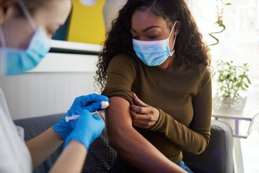 a person wearing a blue face mask with a fear of needles getting a vaccine from a health care worker wearing blue gloves and a face mask