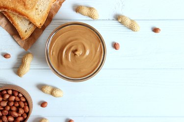 creamy peanut butter and peanuts beans on wooden background top view